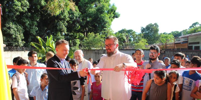 Stifter Bernd Jäger und Pfarrer Peter Eckstein durchschneiden symbolisch das rote Band zum Eingang des neuen Waisenhauses.